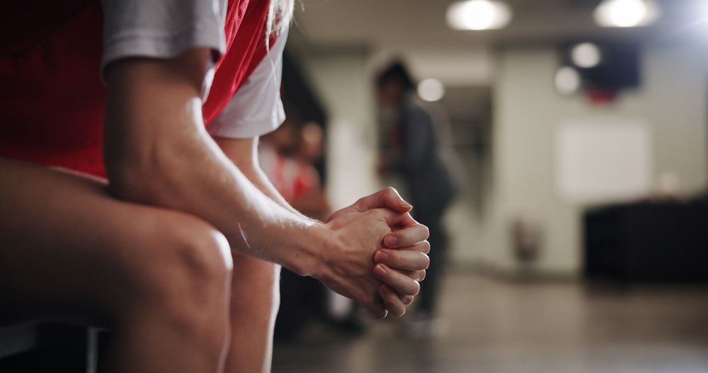 Anxious athlete sitting on a locker room bench with hands clasped, thinking about starting emdr therapy in palm beach, fl with an emdr therapist in palm beach county, fl as part of trauma treatment in palm beach county, fl.
