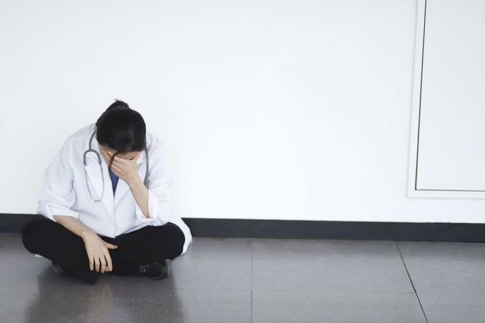 A doctor in a white coat sits on a hospital floor with her head in her hands, representing the cumulative trauma and emotional weight that first responders and medical professionals carry — exactly the kind of unprocessed distress that EMDR therapy in Palm Beach County, FL is designed to address. Like Dr. Mohan and Dr. Robby in The Pitt, many clinicians carry wounds that build silently over time without trauma treatment in Palm Beach County, FL. An EMDR therapist in Palm Beach County, FL can help medical professionals finally begin to heal.