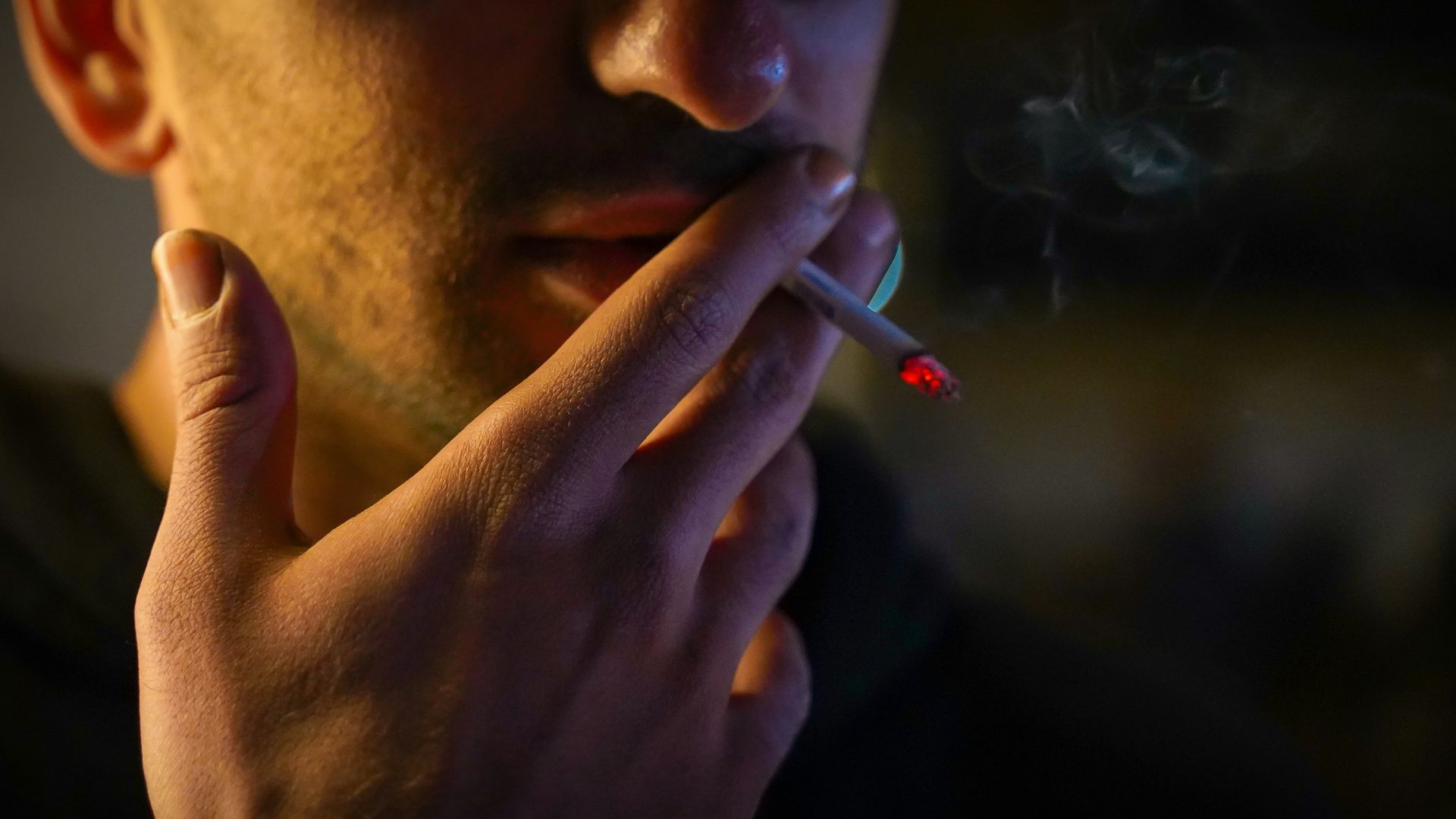 A close-up of a man smoking a cigarette in a dim setting, representing one of the common types of addiction in Palm Beach, FL and the need for addiction counseling in Palm Beach, FL with a skilled addiction therapist in Palm Beach County, FL.