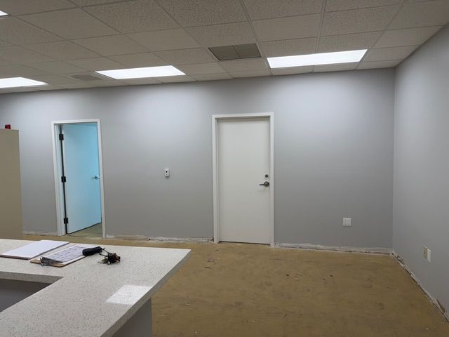 An empty reception area mid-construction, featuring a bare reception desk, unfinished floors, and plain gray walls awaiting transformation. For a trauma therapy in Delray Beach practice like Mangrove Therapy Group, the waiting area sets the tone for the entire therapeutic experience — and this space was about to get a complete overhaul. What you see here is just the starting point of a build-out designed to make every client feel at ease from the moment they walk through the door.