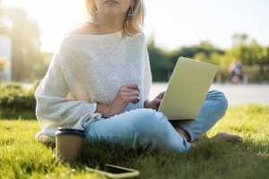 A woman sits cross-legged in the grass with a laptop. This could represent online therapy in Florida and the ability to meet with an online therapist anywhere. Learn more about online trauma therapy and other services today.