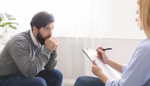 A man sits with his hands together against his mouth. He is listening to a therapist as they write something on their clipboard. This could symbolize the notes an EMDR therapist might make. We offer EMDR trauma therapy in St. Petersburg, FL, virtual emdr therapy in florida, and other services. Contact an online EMDR therapist in Florida for support from Daytona Beach, Orlando, and throughout the state