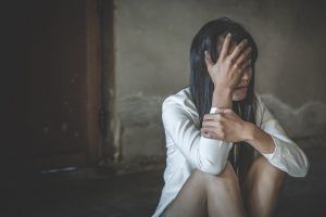 A woman sits in front of a door. She is covering her face with her hand. She appears to be suffering from emotional trauma. We offer support for individuals stuck with their trauma. Contact an EMDR therapist in Tampa, FL for support with EMDR therapy. We serve Miami, St. Petersburg, and offer online EMDR therapy throughout the state.