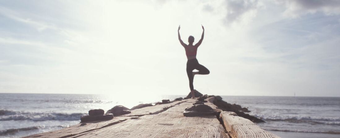 Person standing in a yoga pose near water representing the how our psychologists can help you feel more at peace with your body & physical condition if you live in Florida.