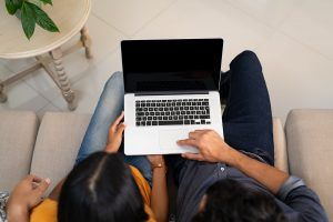 A top down view of a couple typing on a laptop together. This could symbolize the comfort of starting online couples counseling in Florida. Learn more about our services including online marriage counseling in Florida by contacting an online therapist in Florida today! 33704