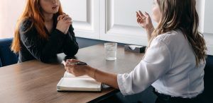 A person sits across a desk from a woman gesturing with her hands. This could represent the support DBT in St. Pete, FL can offer. Learn more by contacting a DBT therapist in Tampa, FL or search “DBT therapist in St. Petersburg, FL” today.
