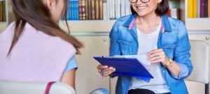A woman smiles while sitting across from a girl and holding a clipboard. Learn how a Tampa therapist can help you along your therapy journey. Learn more about the support a St. Pete therapist can offer by searching for “therapy tampa, fl” today.
