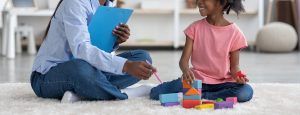 A person holding a clipbaord points to toy blocks as a child plays with them. Learn more about the benefits of PCIT therapy in Tampa, FL by connecting with a PCIT therapist in Tampa, FL.