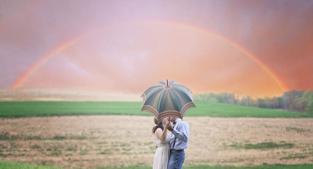 A couple holding an umbrella kiss under rainbow. This represents the love marriage counseling in Tampa, FL can cultivate. Contact a couples therapist in Saint Petersburg, FL for support today!