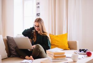 A young woman sits on her living room couch as she smiles at something on her laptop. This could represent the cozy places one can start online EMDR therapy in Florida. We offer support with online EMDR therapy in Florida and other services to help you overcome trauma. Contact an EMDR therapist in Tampa, FL today.