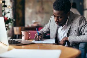 A man writes on paper while sitting in front of a laptop. This could represent completing psychological testing in Tampa, FL. Learn more about Florida counseling and evaluation services by searching for a psychoeducational evaluation in Tampa, FL today. 