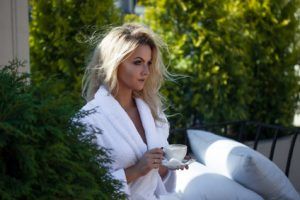 Beautiful young woman in Bathrobe sitting on the terrace and drink coffee