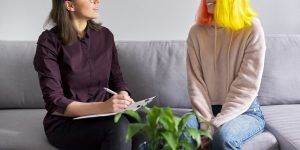 A person with a clipboard smiles while sitting next to a teen. Learn more about how a therapist for teens in Atlanta, GA can offer support. We offer online therapy for teens, in person counseling fore teens, and more.