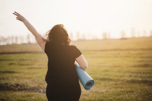 A woman holds a peace sign up while walking with a yoga mat. Treatment for depression in Atlanta, GA can offer support in overcoming past pain. Learn more about our services by contacting an online depression therapist in Atlanta, GA or search "therapist near me for depression" today.