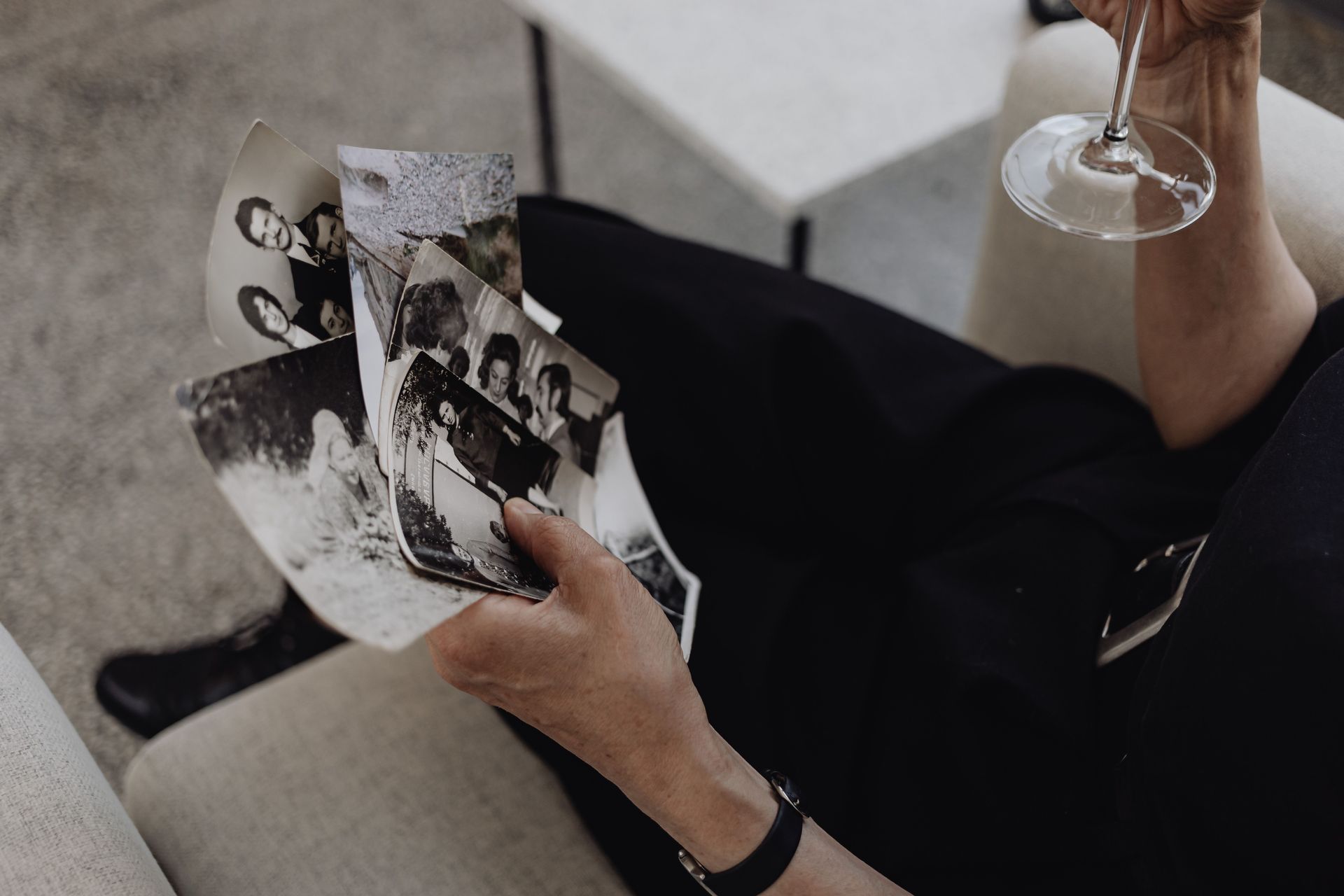 A woman holding old family pictures while drinking a glass of wine. 